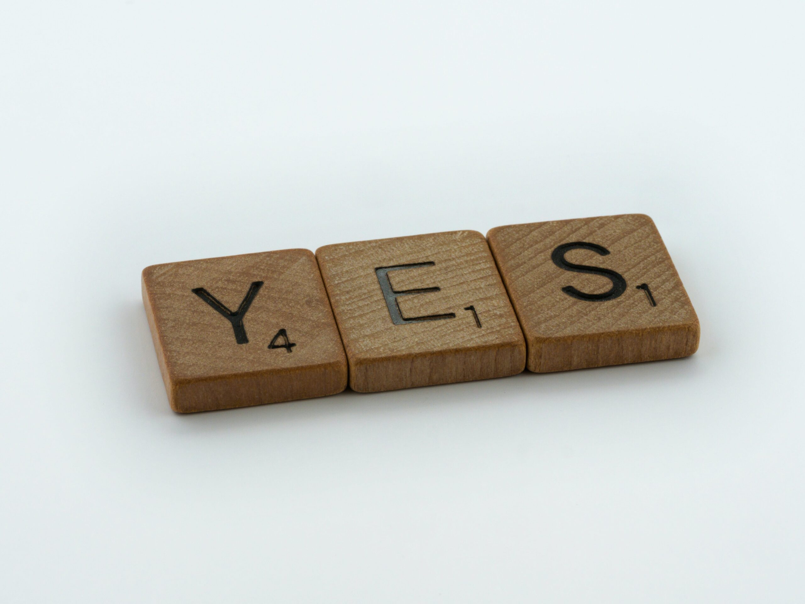 Drei Scrabble-Steine aus Holz bilden das Wort "Yes".