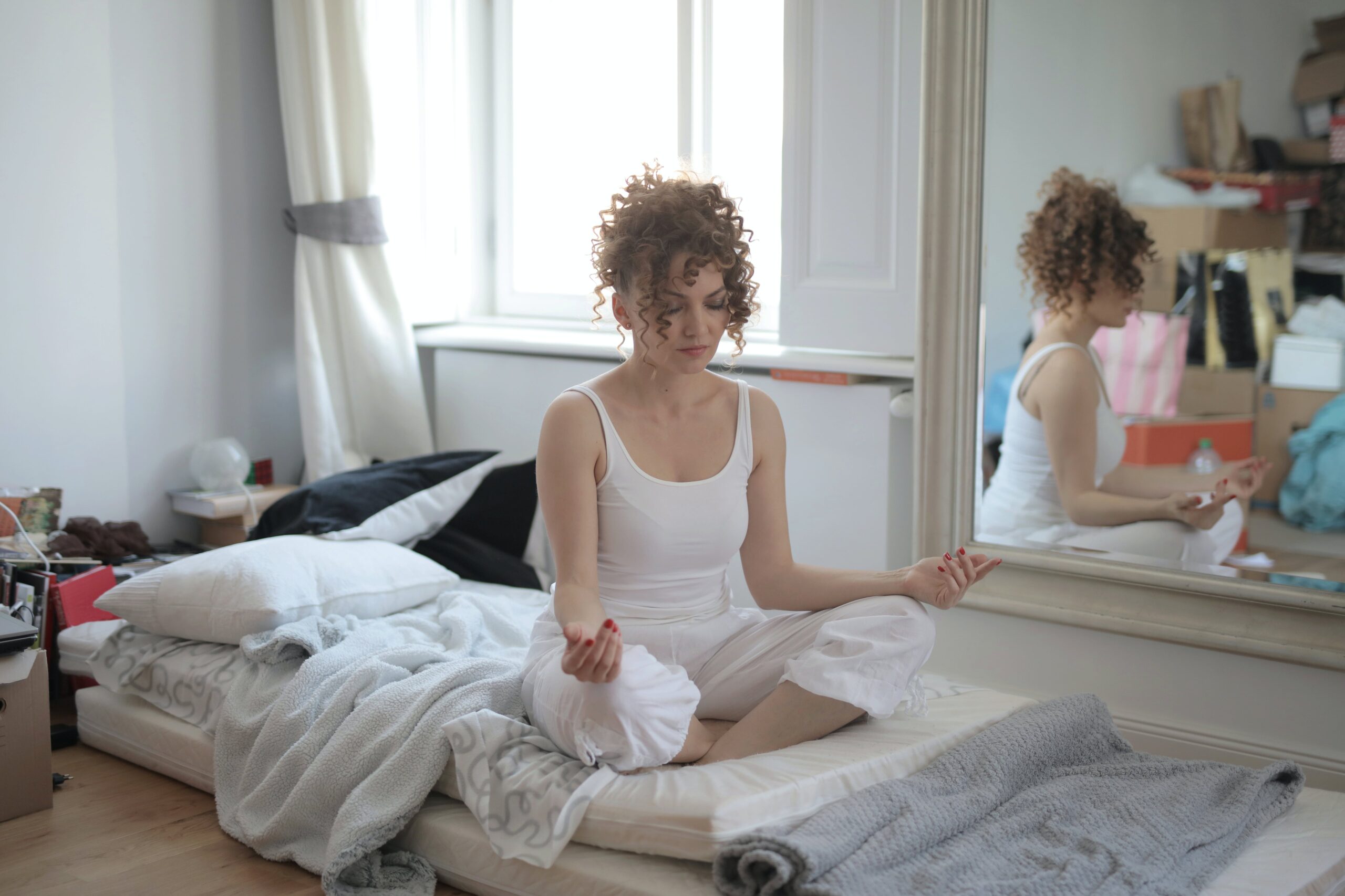 Eine Frau sitzt im Schneidersitz im Bett und meditiert.