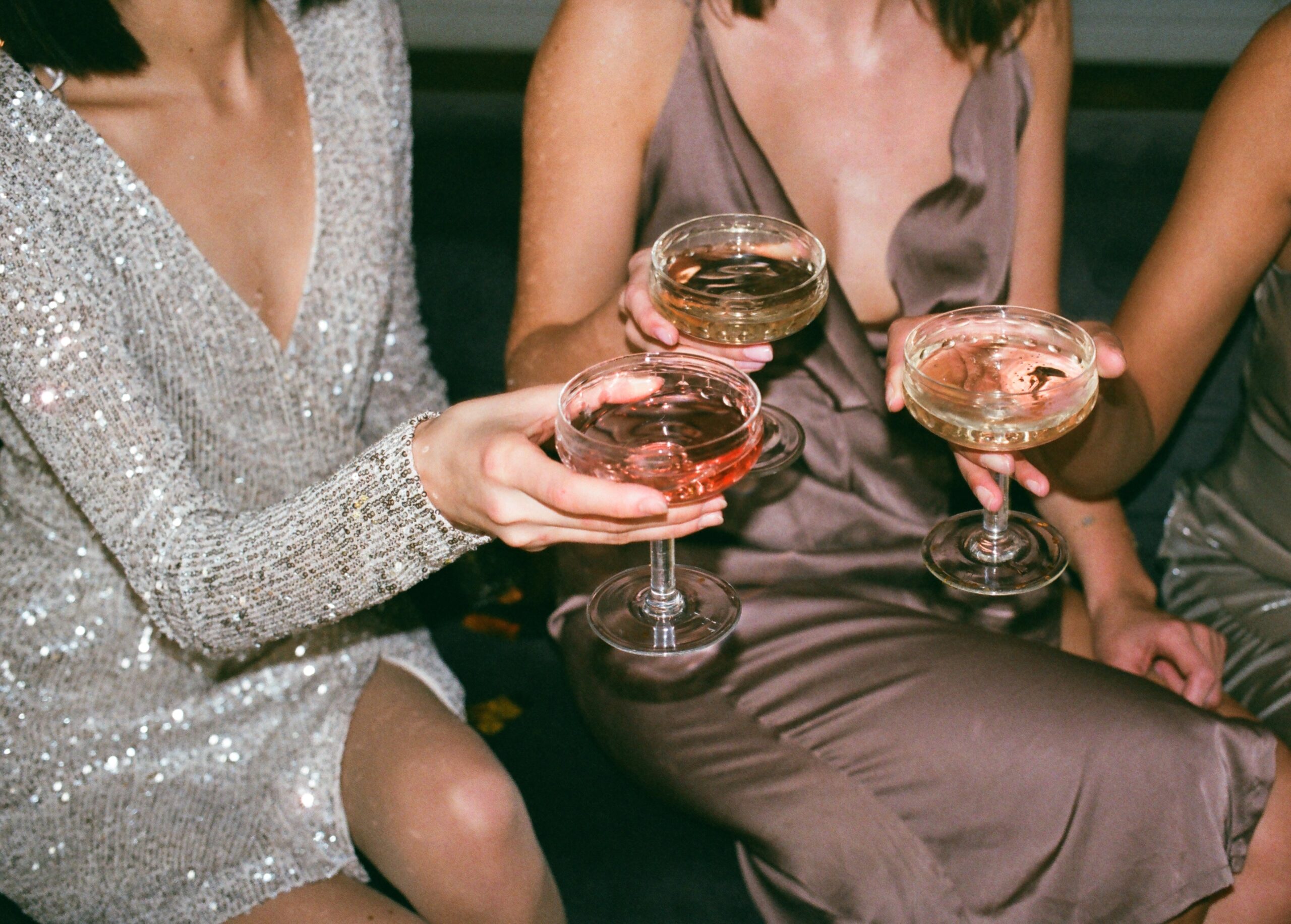 Drei Frauen in Abendkleidern stoßen mit Cocktailgläsern an.