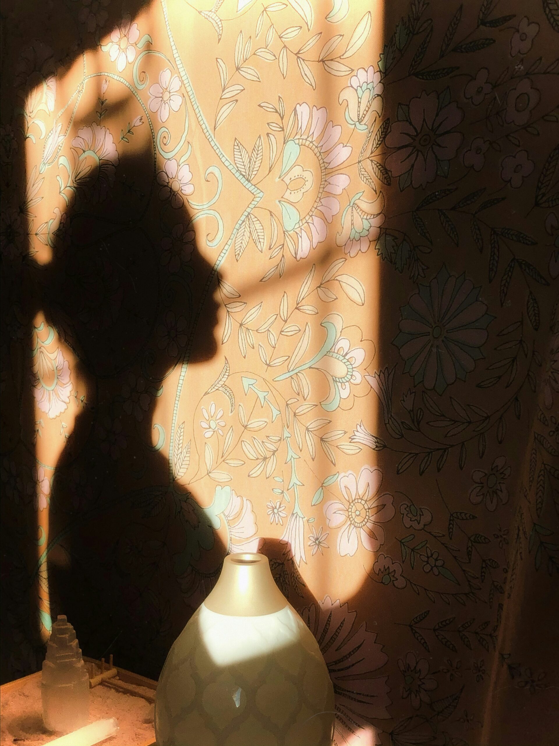 Der Schatten einer Frau auf einem gelb geblümten Vorhang.