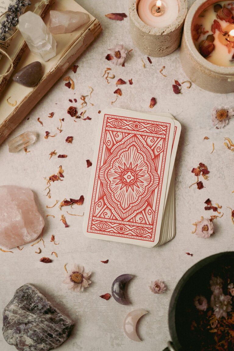 Ein Deck Tarot Karten liegt zwischen Kristallen und Blüten auf dem Tisch.